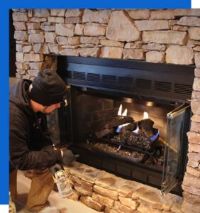 A technician servicing a gas fireplace surrounded by stone, demonstrating expertise from Precision Energy LLC in Everett, WA.