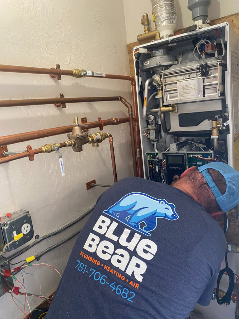 A Blue Bear Plumbing, Heating, & Air technician servicing a tankless water heater system in Norwell, MA.