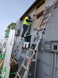 An HVAC technician on a ladder servicing a wall-mounted heating and cooling unit for HP Mechanical LLC in Santa Rosa, CA.