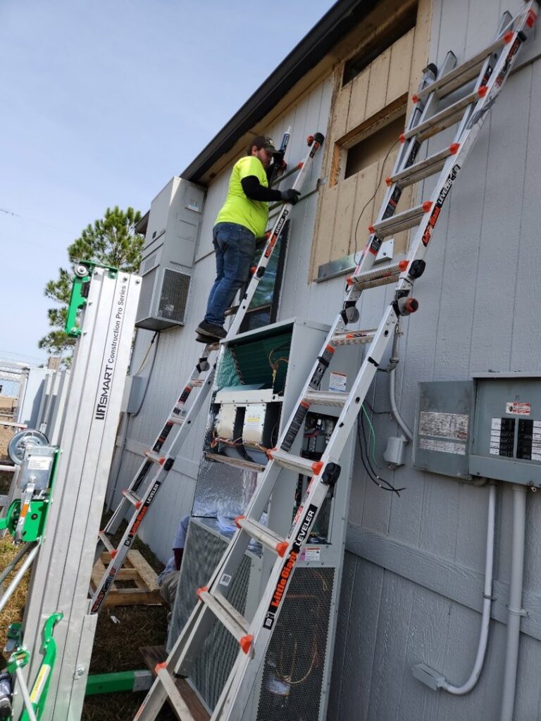 An HVAC technician on a ladder servicing a wall-mounted heating and cooling unit for HP Mechanical LLC in Santa Rosa, CA.