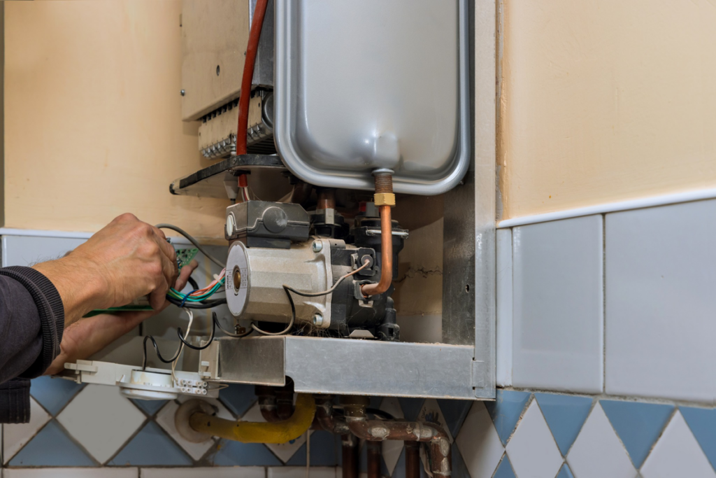 A technician servicing a wall-mounted boiler or water heater at Vassar's Service of Richmond in Richmond, VA