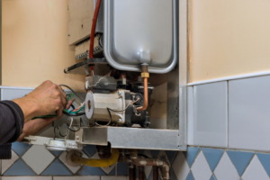 A technician servicing a wall-mounted boiler or water heater at Vassar's Service of Richmond in Richmond, VA
