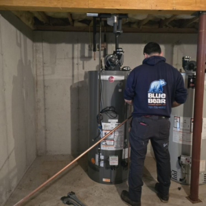 A Blue Bear Plumbing, Heating, & Air technician servicing a water heater in a basement in Norwell, MA.