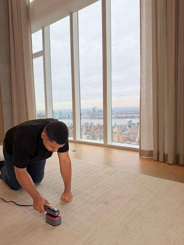 A technician from Cosmo Carpet Cleaning spot cleaning a light-colored carpet in a high-rise apartment in Princeton, NJ.