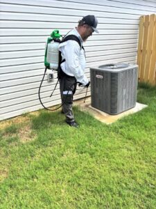 A Diamond Pest Solutions technician in Conway, AR, using a backpack sprayer to treat around an outdoor AC unit for pest control.