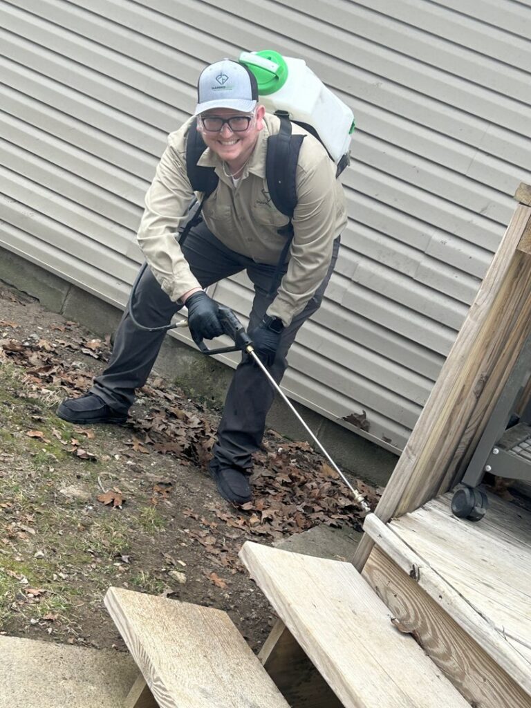 A Diamond Pest Solutions technician in Conway, AR, applying pest control treatment around a wooden deck and stairs.