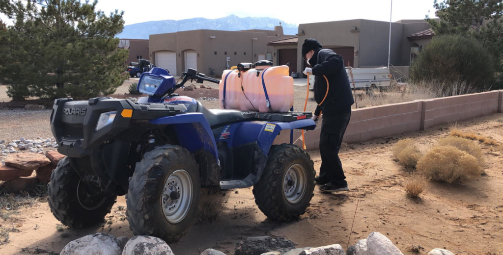 A technician operating an ATV with a spray tank for pest control treatment at Ecotec Pest Control in Rio Rancho, NM.