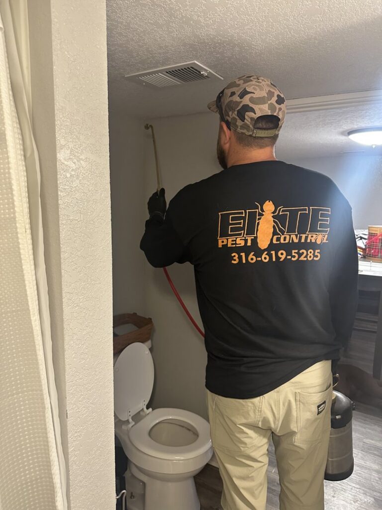 A pest control technician spraying inside a bathroom for pests by Elite Pest Control in Maple Grove, MN.