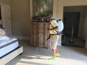 A technician from Johns Creek Carpet Cleaner spraying a bedroom carpet with a backpack sprayer in Johns Creek, GA.
