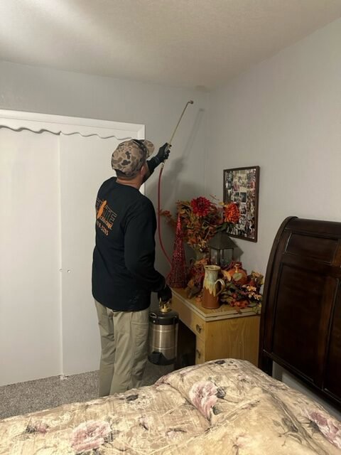 A technician from Elite Pest Control spraying for pests inside a bedroom in Maple Grove, MN.