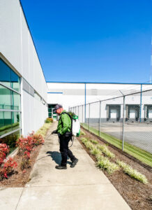A Noosa Pest Management, LLC technician applying pest control treatment with a backpack sprayer along a building exterior in Columbia, SC.