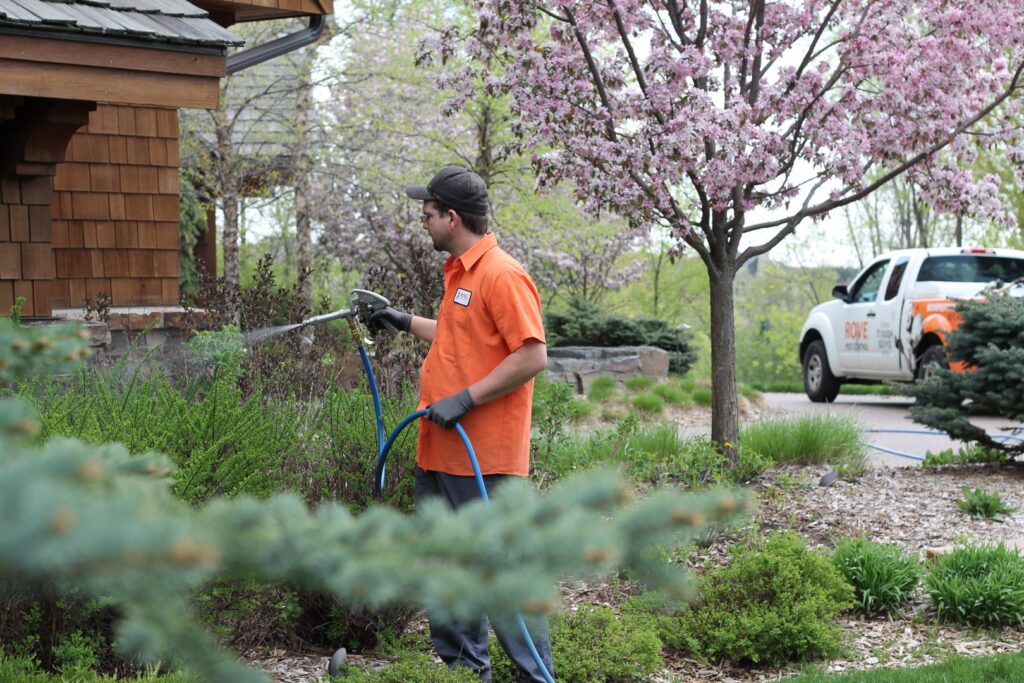 A technician spraying bushes and plants around a residential house for pest control by Pest Free Rochester in Rochester, MN.