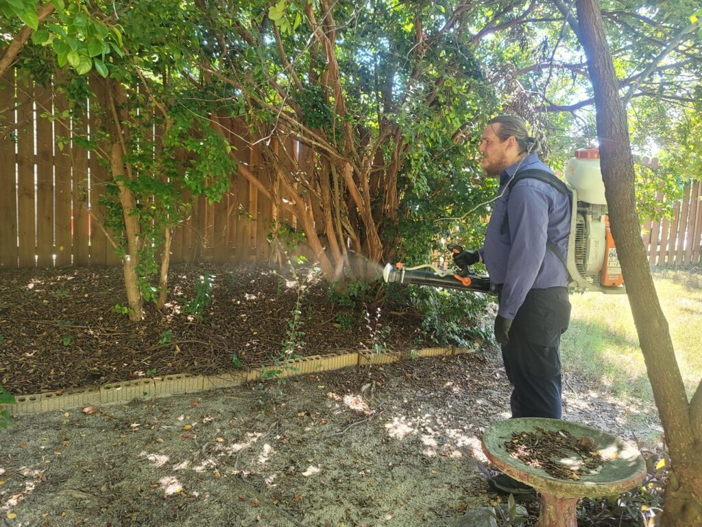 A technician performing mosquito control treatment on bushes in a yard for Stokes Mosquito and Pest Services in North Augusta, SC.