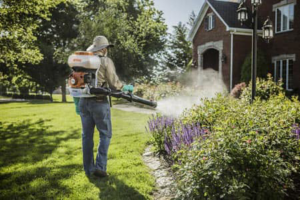 A pest control technician spraying bushes in front of a house, performing a service for Pest Control Consultants in Sycamore, IL.