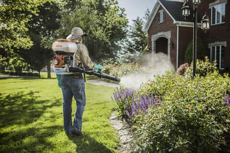 A pest control technician spraying bushes in front of a house, performing a service for Pest Control Consultants in Sycamore, IL.