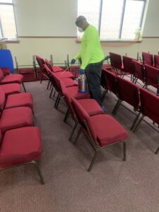 A technician spraying chairs with a treatment solution in a hall, demonstrating services by Pest 2 Rest Pest Control LLC in Milwaukee, WI.
