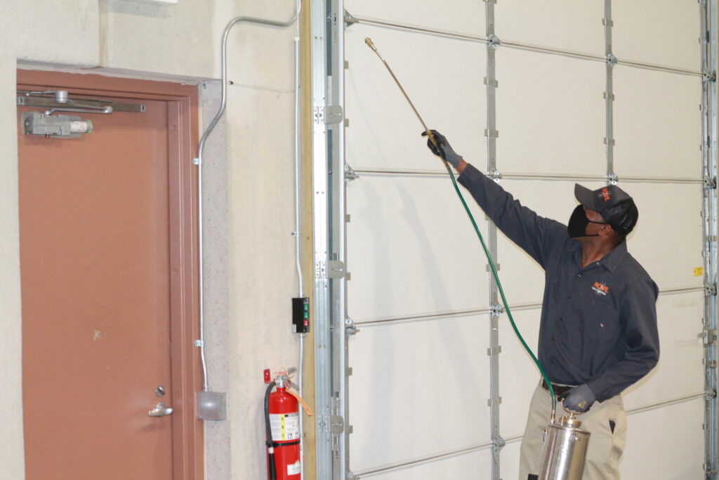 A technician spraying inside a commercial building near a garage door for Pest Free Rochester in Rochester, MN.