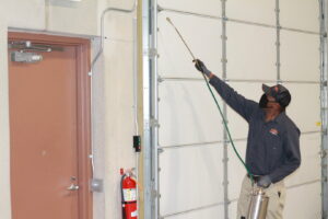 A technician spraying inside a commercial building near a garage door for Pest Free Rochester in Rochester, MN.
