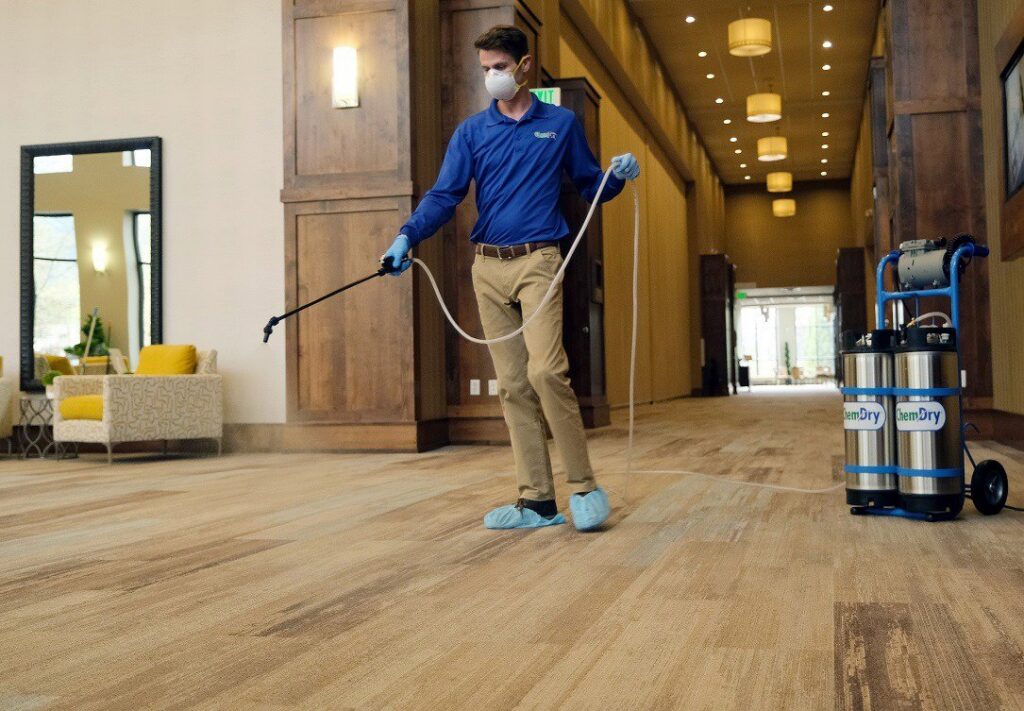 A Brimley's White Glove Chem-Dry technician sprays a large commercial carpeted area during a cleaning service in Mesa, AZ.