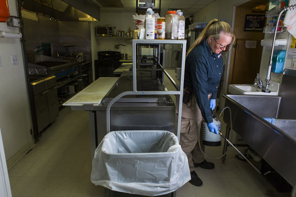 A pest control technician spraying in a commercial kitchen for American Pest Management in Saint Petersburg, FL.