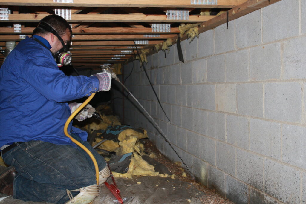 A Capital Pest Services technician wearing a respirator and spraying a crawl space for pests in Raleigh, NC.