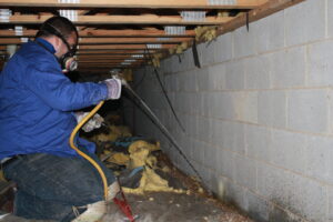 A Capital Pest Services technician wearing a respirator and spraying a crawl space for pests in Raleigh, NC.