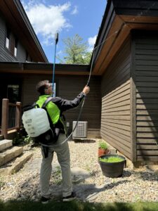 A Green Harmony technician applying pest control treatment under the eaves of a house in Oconomowoc, WI.