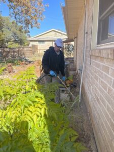 A Blessed Pest Control technician applying an exterior pest treatment near an AC unit of a house in San Antonio, TX