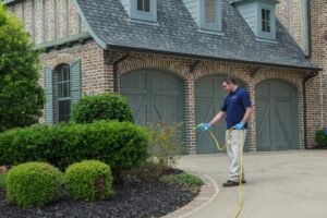 A Berrett Pest Control Denver technician spraying liquid pest treatment around a home's exterior in Denver, CO.