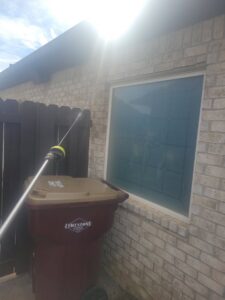 A technician from A Plus Pest Control spraying an exterior wall near a trash can in Huntsville, AL.