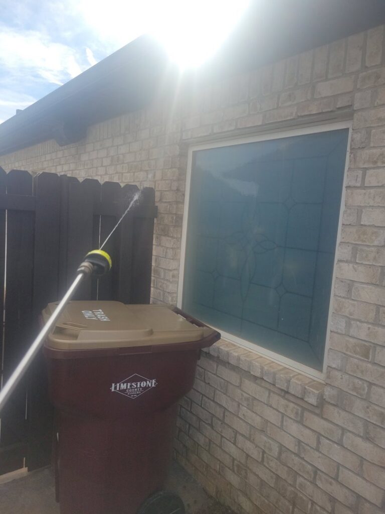 A technician from A Plus Pest Control spraying an exterior wall near a trash can in Huntsville, AL.