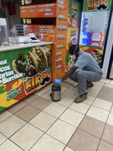 A pest control technician wearing a mask and gloves, applying treatment in a commercial kitchen for Illuminating Pest Control in Johns Creek, GA.