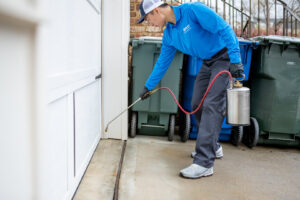 A Pest Authority Des Moines technician spraying the base of a garage door with a pump sprayer in Des Moines, IA.