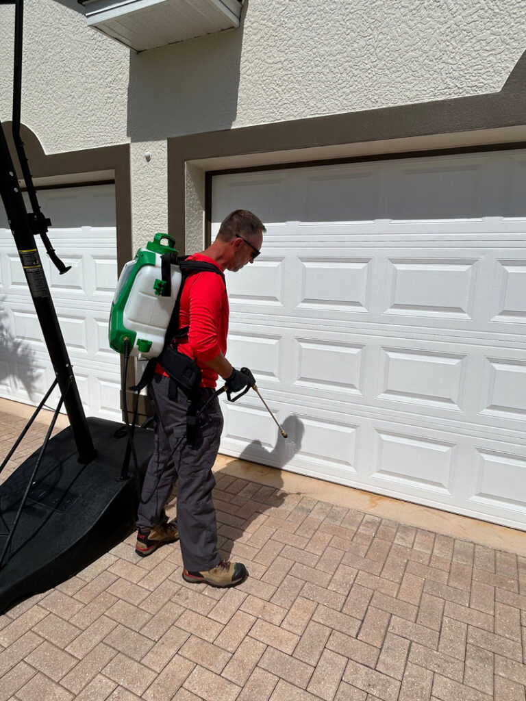 A Paske Pest Control & Wildlife Solutions technician applying pest treatment near a residential garage door in Cape Coral, FL.