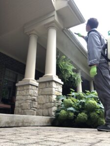 A Bayer Pest Control technician using a backpack sprayer to treat the eaves of a house porch for pests in Dayton, OH.