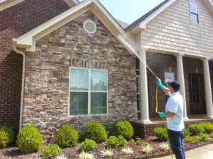 A technician from A Plus Pest Control spraying the exterior of a house for pest control in Huntsville, AL.