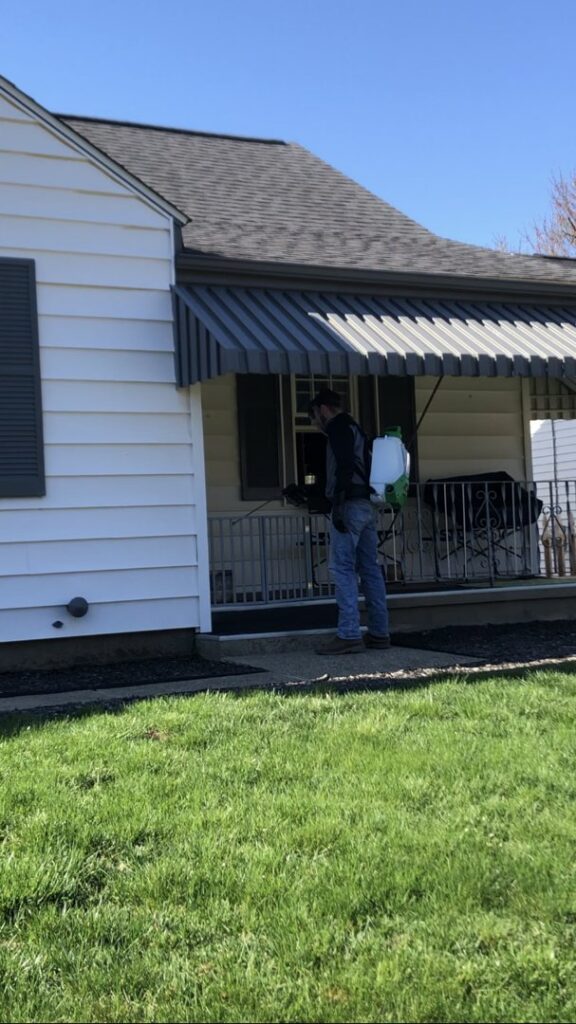 A technician using a backpack sprayer to treat the exterior of a house for pests by Antix Pest Control in Canton, OH.