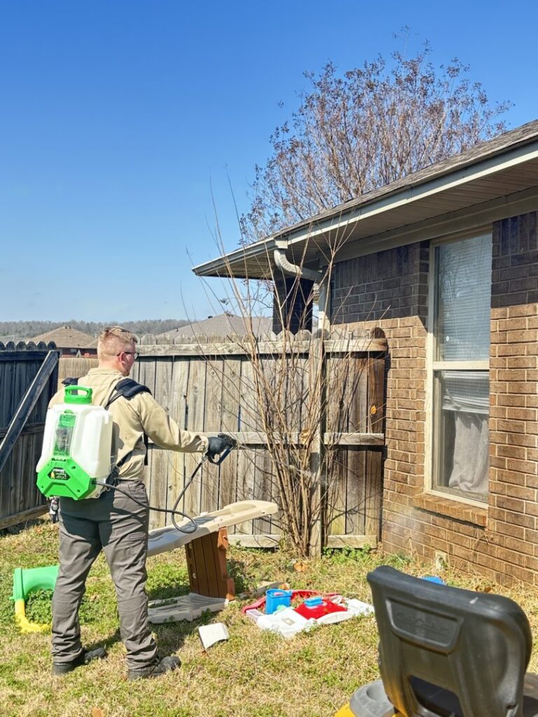 A Diamond Pest Solutions technician in Conway, AR, spraying the exterior of a house near a fence for comprehensive pest control.