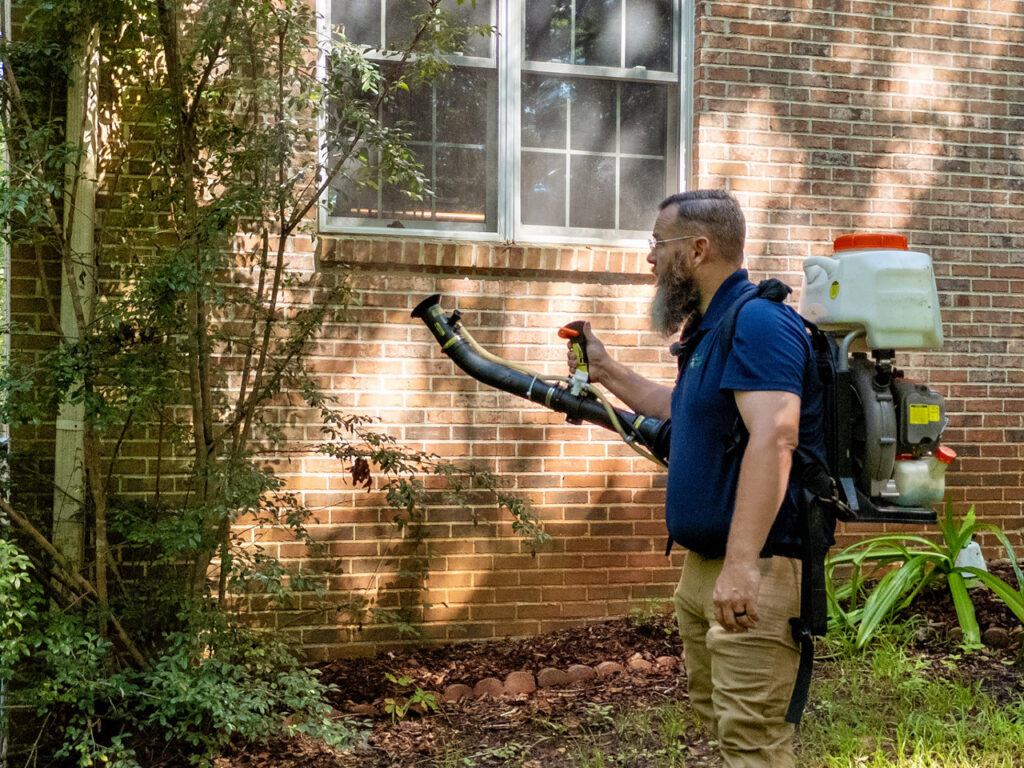 A Pest Magic Pest Control technician spraying the exterior of a house with a backpack sprayer in Forsyth, GA.