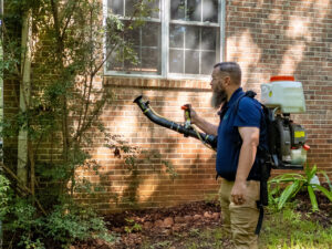A Pest Magic Pest Control technician spraying the exterior of a house with a backpack sprayer in Forsyth, GA.