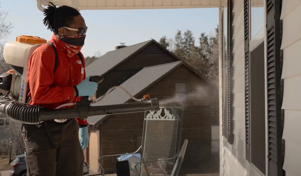A pest control technician spraying the exterior of a house from a porch for Richmond Pest Control in Richmond, KY.