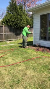 A technician spraying the exterior of a residential house for pest control by Global Green Termite & Pest Control LLC in Hampton, VA.