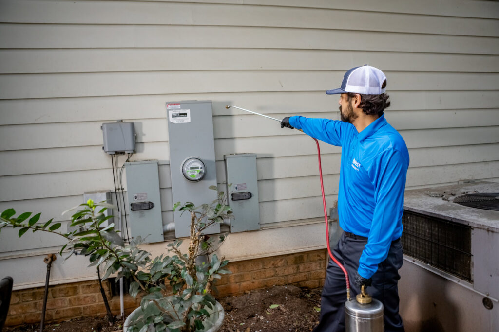 A Pest Authority Des Moines technician spraying the exterior foundation of a house with a pump sprayer in Des Moines, IA.