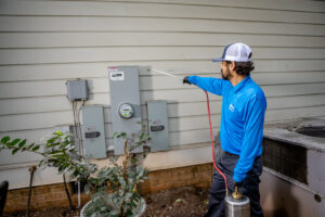 A Pest Authority Des Moines technician spraying the exterior foundation of a house with a pump sprayer in Des Moines, IA.