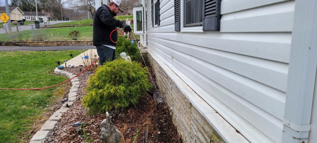 A pest control technician spraying the exterior foundation of a residential home for pest prevention by Pest In Class Exterminating in Johnson City, TN.
