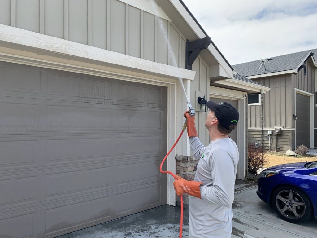 A PestEx Idaho technician spraying the exterior of a house near a garage door in Boise, ID, performing pest control.