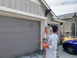 A PestEx Idaho technician spraying the exterior of a house near a garage door in Boise, ID, performing pest control.