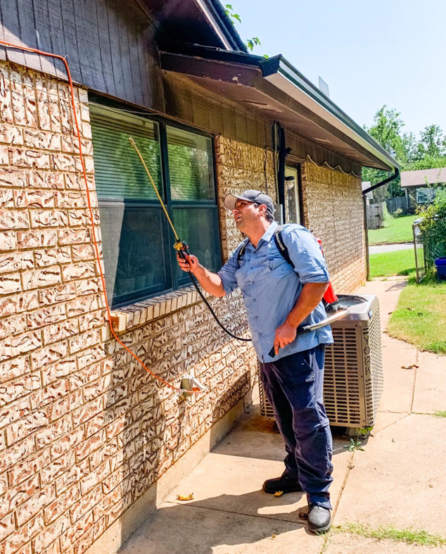 A pest control technician spraying the exterior brick wall of a house for Vanguard Pest Solutions in Oklahoma City, OK