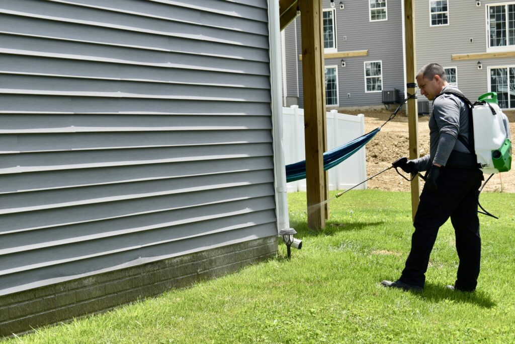A Bye Bye Pest Solutions technician spraying the exterior foundation of a house for pest control in Hanover, PA.
