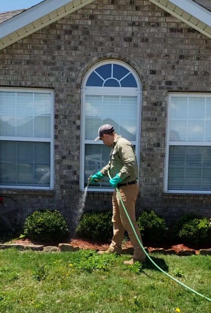 A technician spraying the foundation of a house for pest control by Defender Wildlife & Pest Control in Rogers, AR.